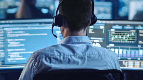 Back of an IT worker with headset looking at two screens